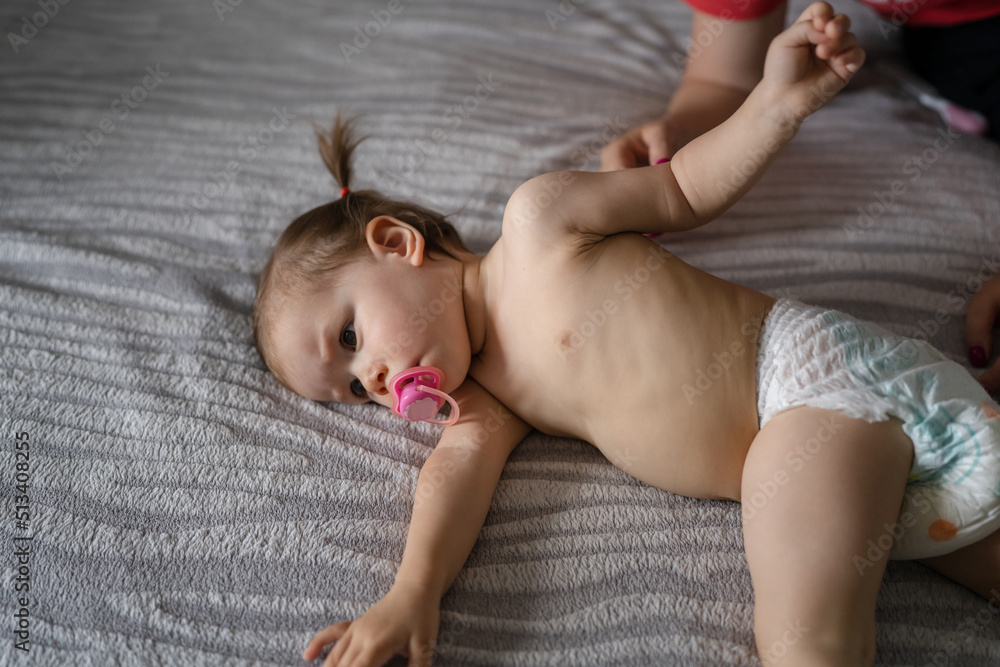 One female toddler in diapers lying down on bed in bedroom at home Childhood concept - obrazy, fototapety, plakaty 