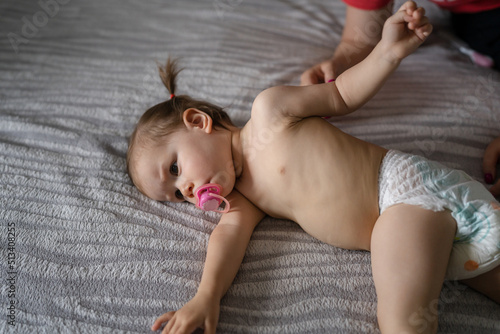 One female toddler in diapers lying down on bed in bedroom at home Childhood concept