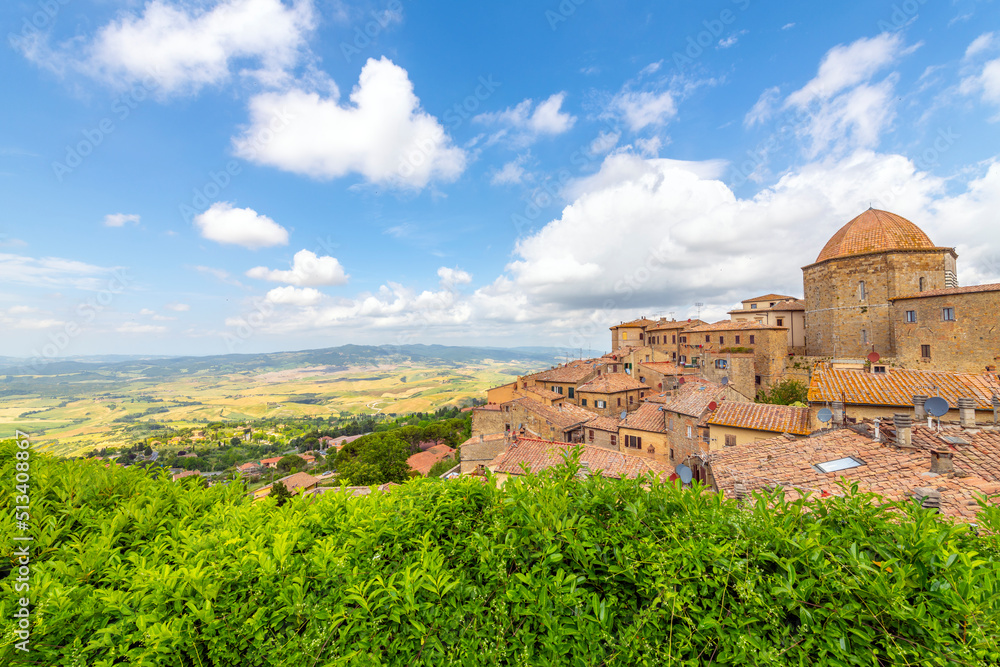 View of the colorful hills of Tuscany and the medieval hilltop town of Volterra, Italy, with the duomo and city walls in view.