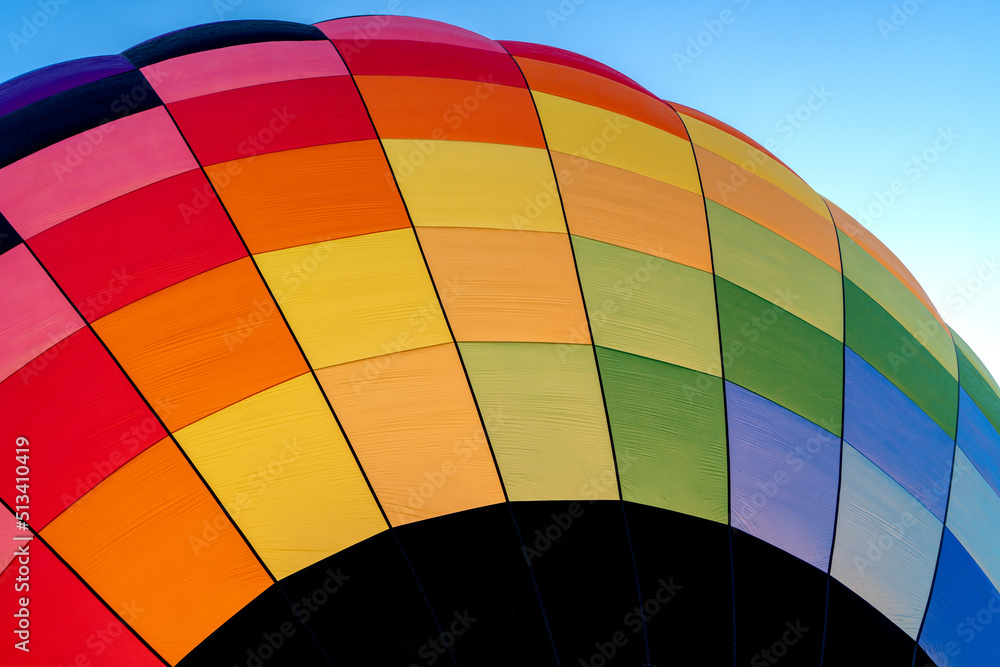 Fototapeta premium A colorful rainbow hot air balloon inflating against a blue sky