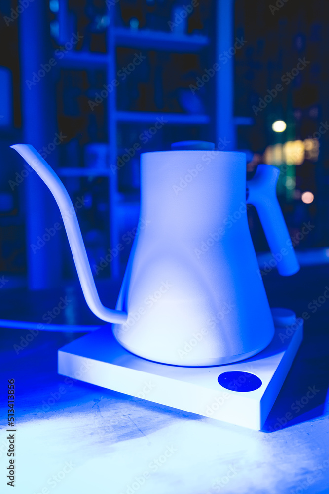 Modern white ceramic electric kettle over a wooden table with dark blue lights in the night Modern white ceramic electric kettle over a wooden table with dark blue lights in the night