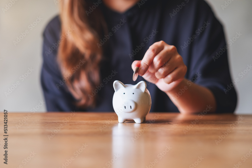 Closeup image of a woman putting coin into piggy bank for saving money concept - obrazy, fototapety, plakaty 