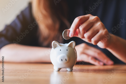 Slika na platnu Closeup image of a woman putting coin into piggy bank for saving money concept