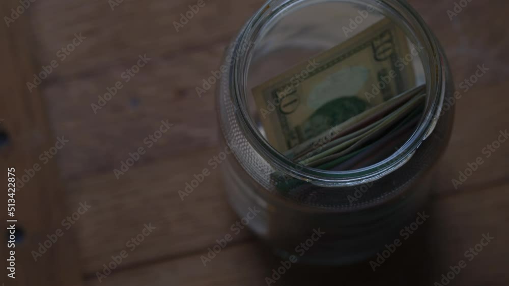 hand Puts American Dollar into a Glass Jar for Storage. Hand puts money in jar hand Puts American Dollar into a Glass Jar for Storage. Hand puts money in jar