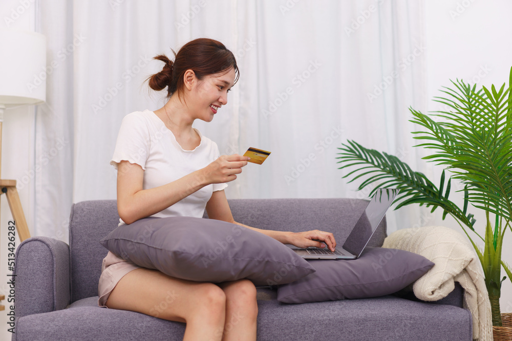 Lifestyle in living room concept, Asian woman holding credit card and use laptop to online shopping Lifestyle in living room concept, Asian woman holding credit card and use laptop to online shopping