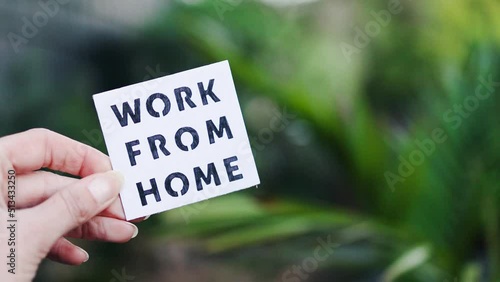 work from home sign being hold in front of out of focus lush green backard, digital nomads working remotely or wfh days during lockdowns photo