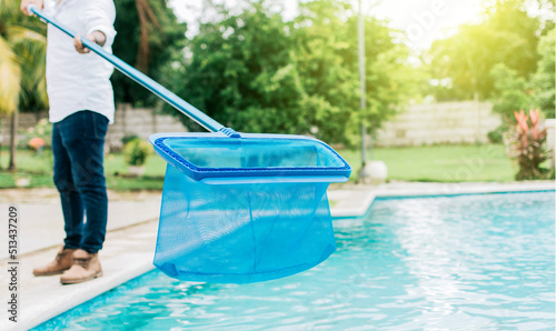 Man cleaning the pool with the Skimmer, A man cleaning pool with leaf skimmer. Person with skimmer cleaning pool, Hands holding a skimmer with blue pool in the background