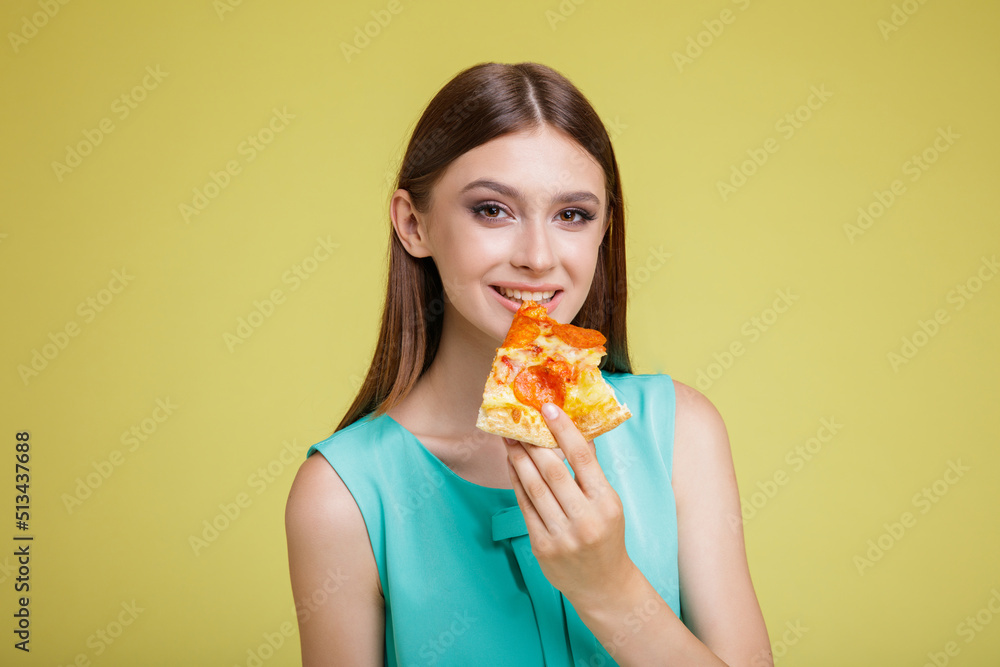 Beautiful young happy woman in a pretty aqua blue dress with posing on yellow background. Slim figure, studio shot. Delicious slice of pizza in hands. Model eats pizza Beautiful young happy woman in a pretty aqua blue dress with posing on yellow background. Slim figure, studio shot. Delicious slice of pizza in hands. Model eats pizza