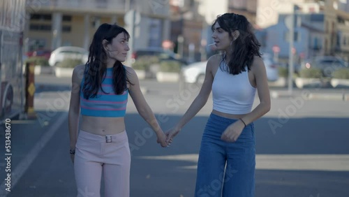 Slomo of two dark-haired girls roller skating on street toward camera photo