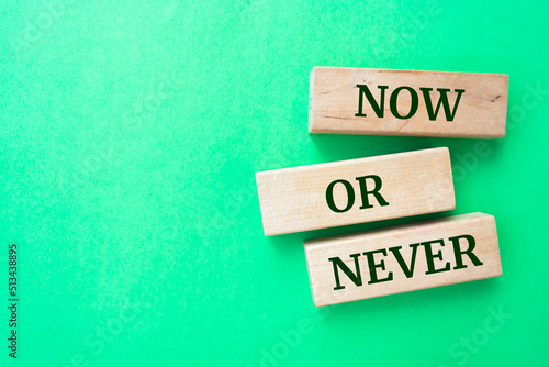 now or never words on wooden blocks on green background.