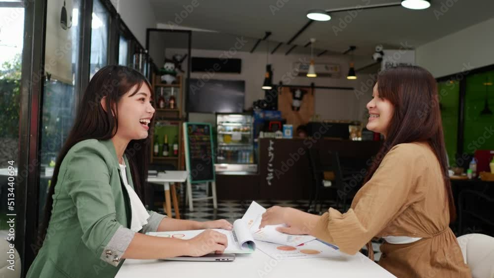 Young woman and her female colleague working on laptop computer and paper work or report in coffee shop, They doing high five with glad in successful Young woman and her female colleague working on laptop computer and paper work or report in coffee shop, They doing high five with glad in successful