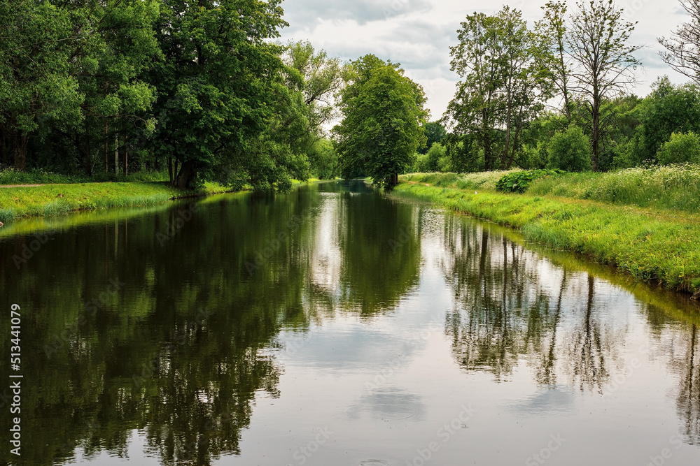 Reflection of trees in the water of a forest river. Green park or forest on the bank of the river in cloudy weather. Northern summer, vacation time, banner or background idea Reflection of trees in the water of a forest river. Green park or forest on the bank of the river in cloudy weather. Northern summer, vacation time, banner or background idea