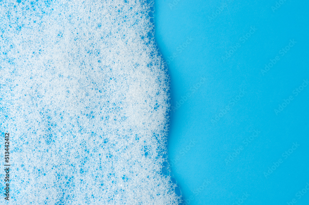 Texture of white foam on a blue background. Cleansing mousse for the face or bath foam or washing powder. Closeup. Copy space - obrazy, fototapety, plakaty 