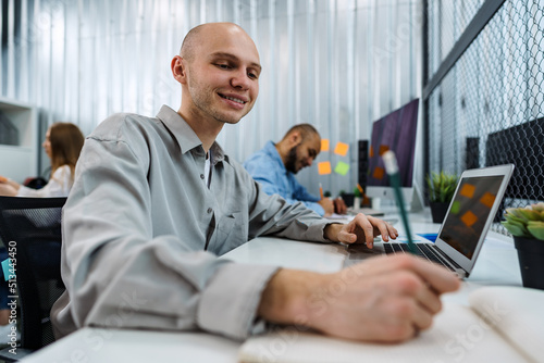Young bald business man sitting at desk in office, working on computer