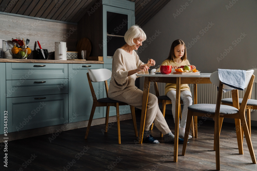 Happy senior woman having breakfast with her granddaughter in kitchen Happy senior woman having breakfast with her granddaughter in kitchen