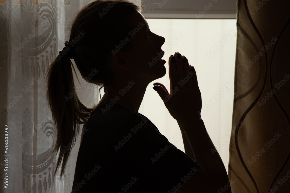Ukrainian girl pray near the window in the dark to God for salvation, prayer