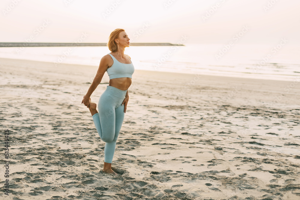 A woman stretches her leg on the beach, prepares for exercises or finishes a workout A woman stretches her leg on the beach, prepares for exercises or finishes a workout