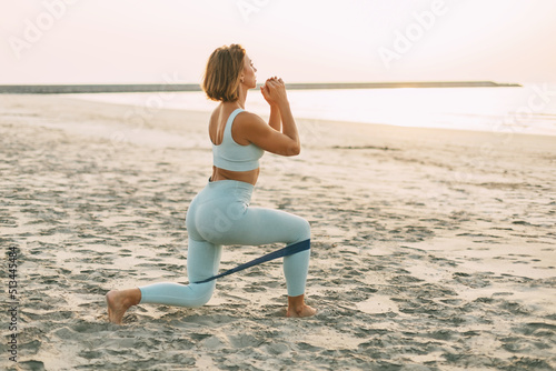 A sporty woman trains with a resistance band, makes lunges.A girl in sportswear trains on the beach