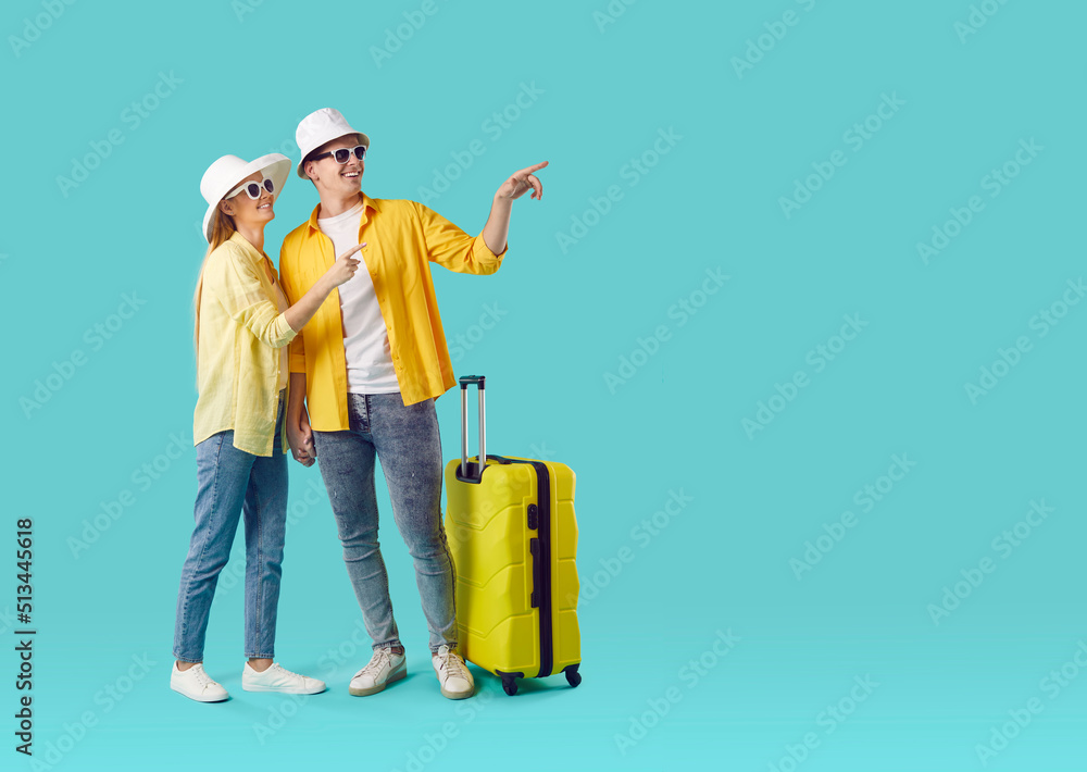 Passenger travel abroad for weekend. Joyful happy couple female and male tourists show on copy space on light blue background. Full length of young man and woman with suitcase near advertising space. Passenger travel abroad for weekend. Joyful happy couple female and male tourists show on copy space on light blue background. Full length of young man and woman with suitcase near advertising space.