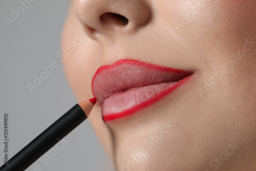 Fotografija Young woman applying beautiful red lip pencil on grey background, closeup