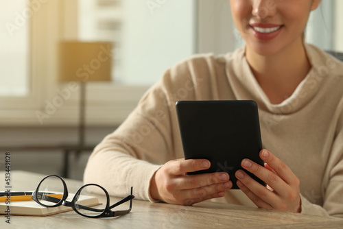 Young woman using e-book reader at wooden table indoors, closeup. Space for text