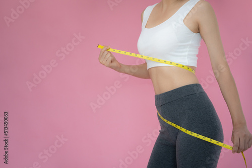 Slim woman in sportswear measures her waist using tape measure on pink background Fototapeta
