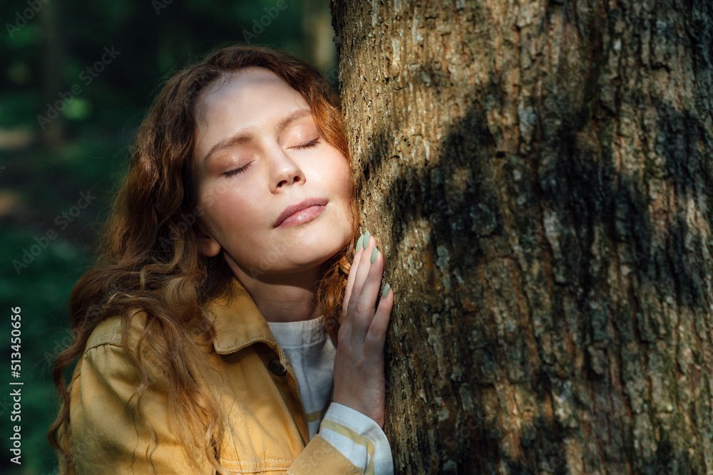 Woman with eyes closed embracing tree in forest Woman with eyes closed embracing tree in forest