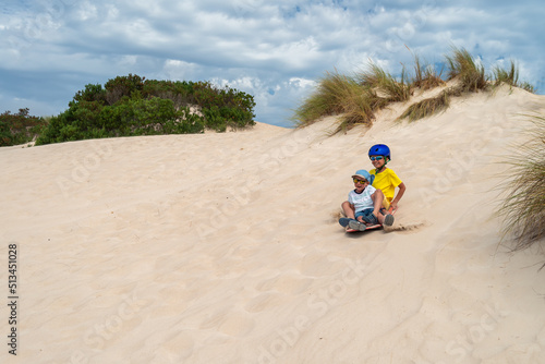 Children having fun while sliding down sand dune on sandboard, Kangaroo Island, South Australia