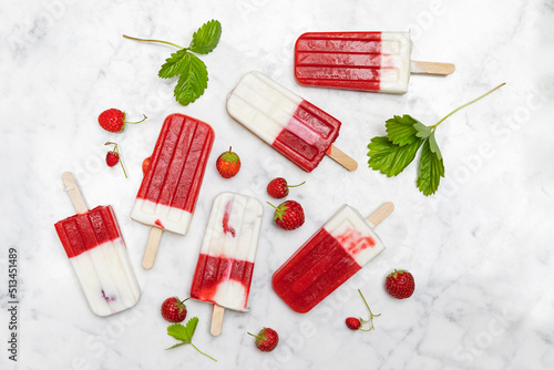 Homemade strawberry-yogurt popsicles flat laid against white marble photo