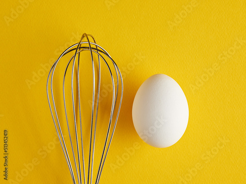 A whisker and a white egg on yellow background. Whisk cooking egg beater mixer whisker.