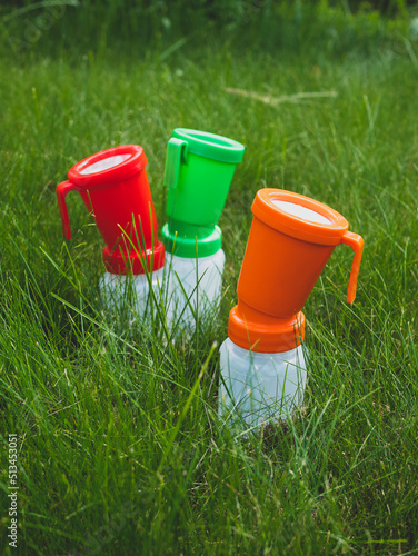 Three colored teat dip cups for cattle on the grass. Concept of hygiene and disinfection of cow's udder. Health care of udder before and after milking