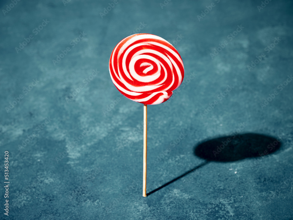 White and red swirl round candy lollipop standing on blue background. Summer concept. White and red swirl round candy lollipop standing on blue background. Summer concept.