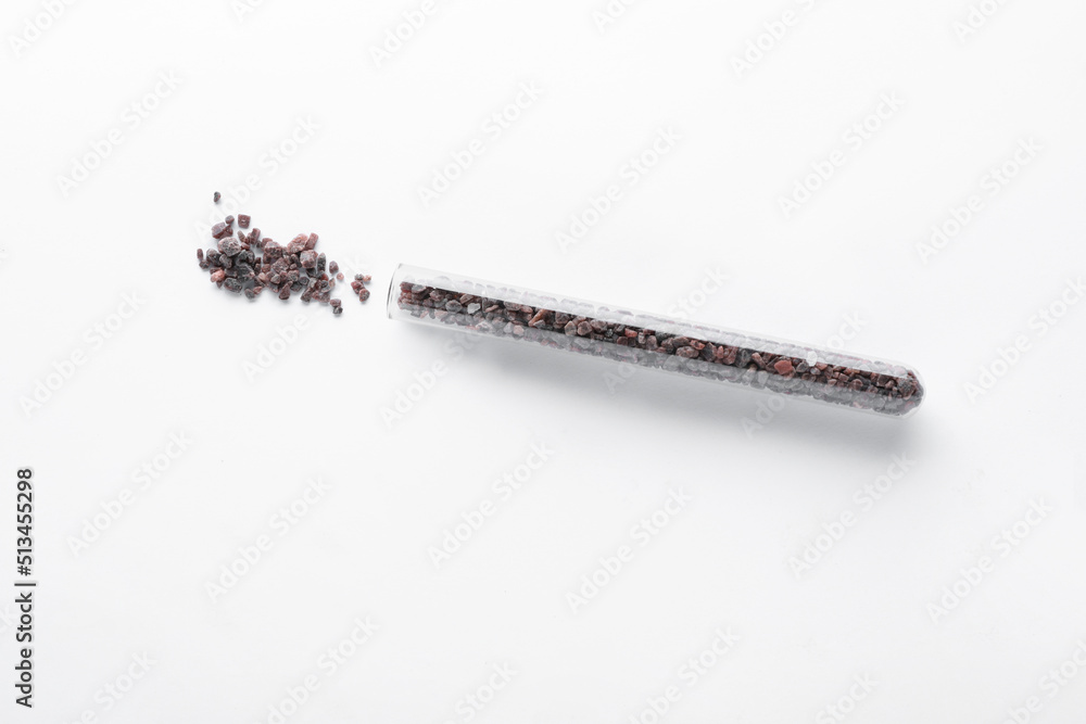 Glass tube with black salt on white background, top view Glass tube with black salt on white background, top view