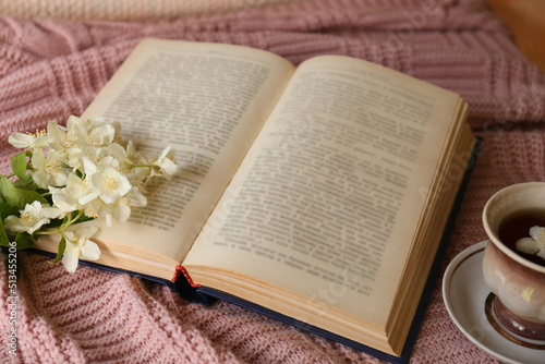 Open book, cup of aromatic tea and beautiful jasmine flowers on pink fabric