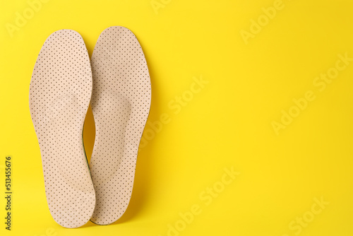 Beige orthopedic insoles on yellow background, flat lay. Space for text