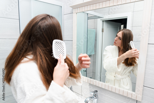 A young woman in a bathrobe combs her hair in front of a mirror. Morning fees with a bathroom