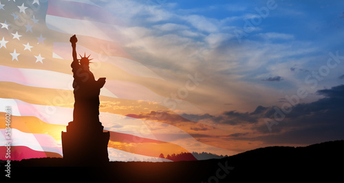 Statue of Liberty with a large american flag and sunset sky on background. Greeting card for Independence Day. USA celebration.