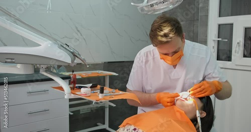 dental office, young doctor stomatologist in mask and sterile gloves treats teeth of client who lies in medical chair