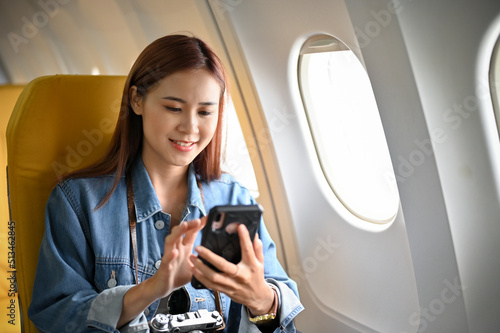 Beautiful asian female passenger sits at the window seat using smartphone during flight. photo