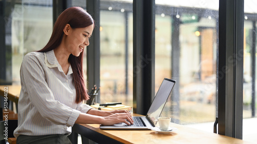 Happy young woman looking at screen working in internet, typing email on laptop computer