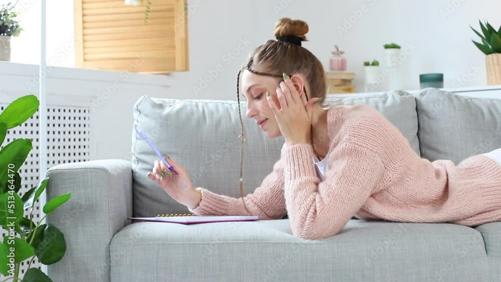 smiling woman and writing in notebook on sofa at home. lazy smiling woman and writing in notebook on sofa at home. lazy