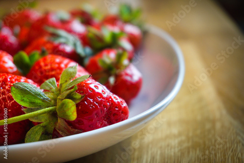 Strawberries on plate, wooden table - close-up, defocused background.