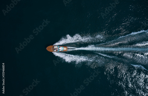 Modern wooden boat in a classic design, moving on water, aerial view. Luxurious wooden boat with people moves on dark water top view. Italian classic wooden boat fast movement on the water top view. photo