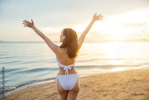 Back view. Happy young woman in bikini swimsuit posing relax in tropical sea beach with arms raised, Asian female raised hand up on summer holiday travel © sorapop