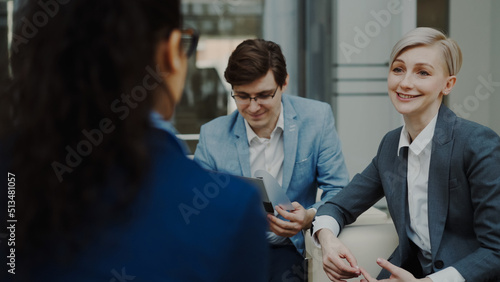 Businesswoman talking and duscussing future deal with business partners sitting on couch in modern office center indoors
