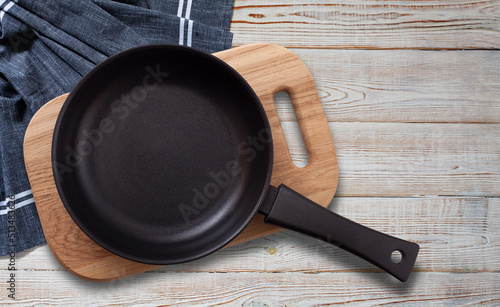 Black fry pan and board with napkin on wooden table. Top view mockup