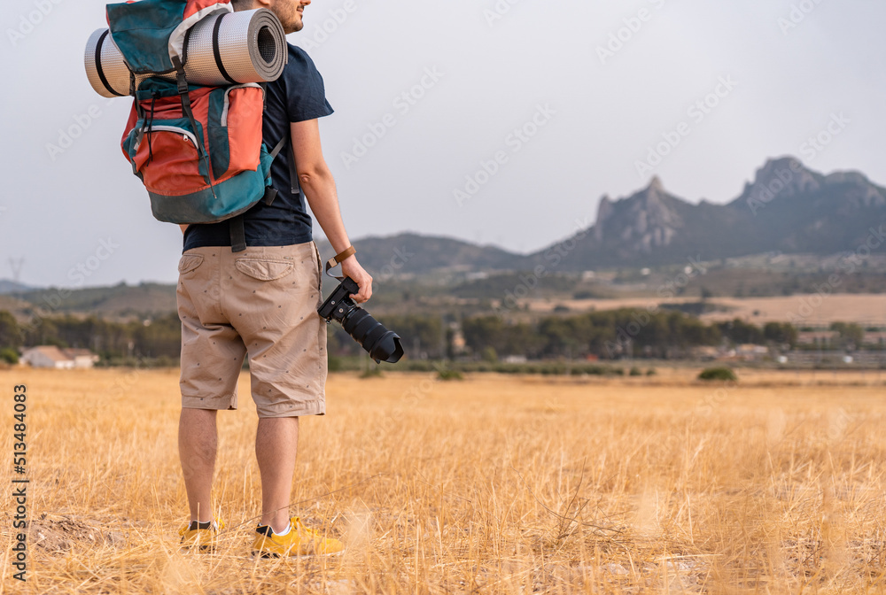 Hombre con mochila de acampada y esterilla, con su cámara de fotografía, en  un paisaje de prados y montañas. Fotografía horizontal con espacio para  texto. Stock Photo