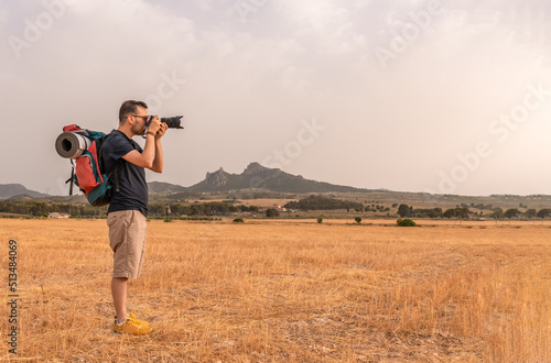 Hombre nómada con la mochila y esterilla, fotografiando el paisaje de prados y montañas. Fotografía horizontal con espacio para texto. © Ezequiel Martínez
