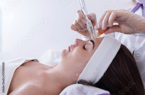 close up of Cosmetologist,beautician applying facial dermapen treatment on face of young woman customer in beauty salon.Cosmetology and professional skin care, face rejuvenation. photo