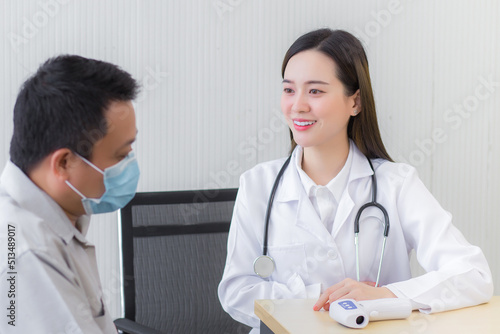 Professional young Asian female doctor talking with a man patient about his pain and symptom while they put on a face mask to prevent Coronavirus disease on table at the examination room in hospital.